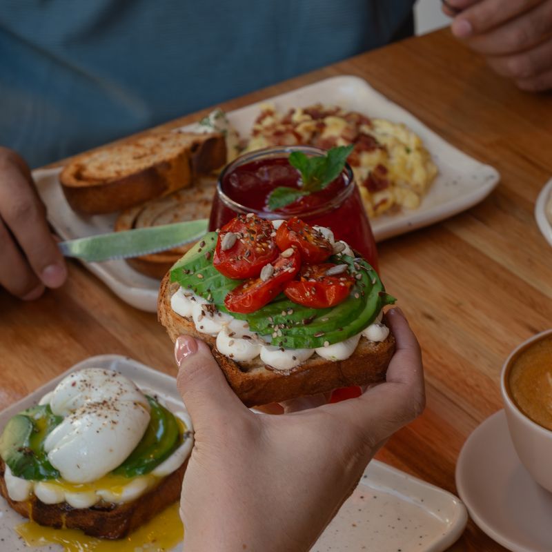 Mesa de desayuno con tostada de palta y tomates, huevos revueltos, tostadas de roll de canela y café